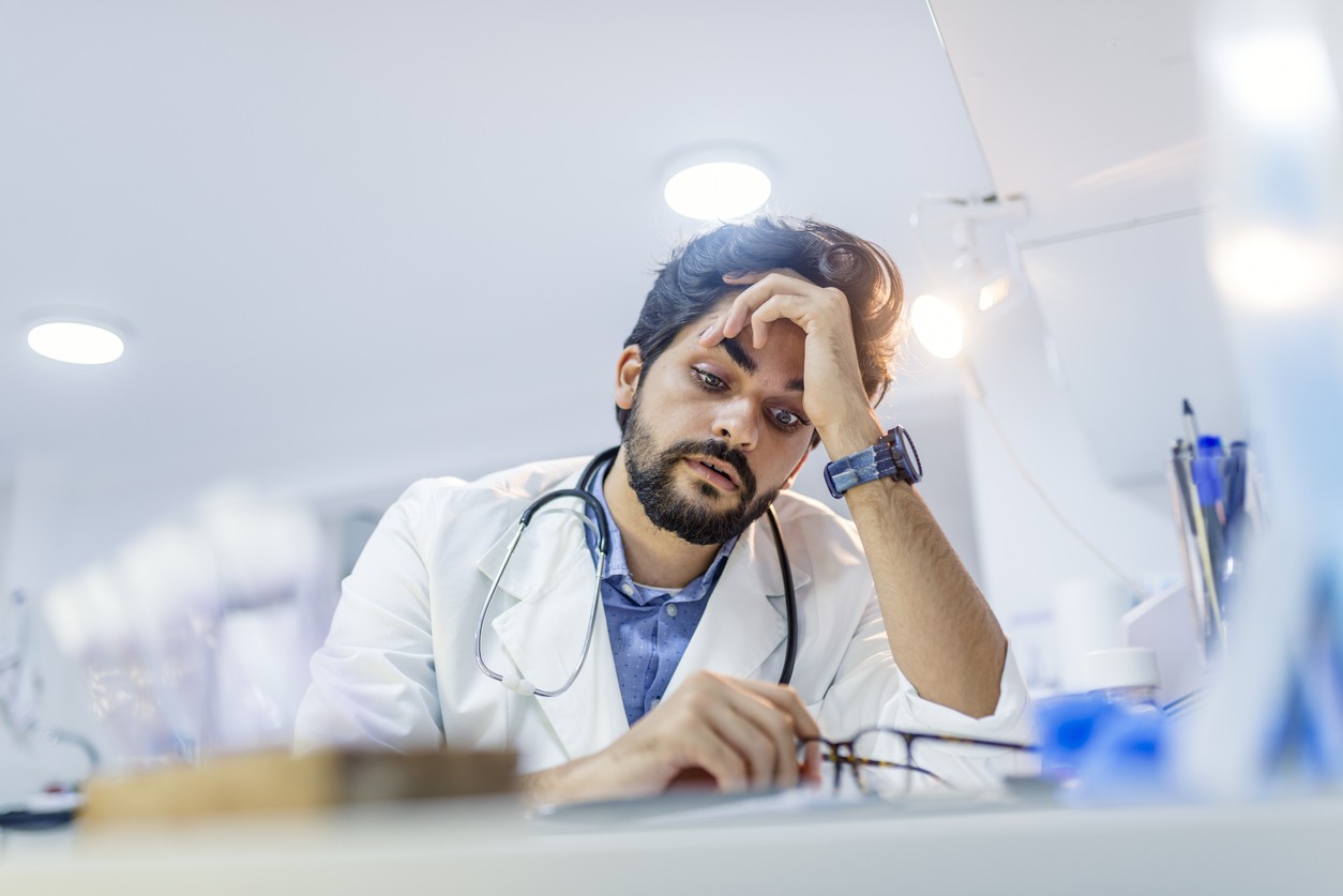 Stressed male doctor sat at his desk. Mid adult male doctor working long hours. Overworked doctor in his office. Not even doctors are exempt from burnout .