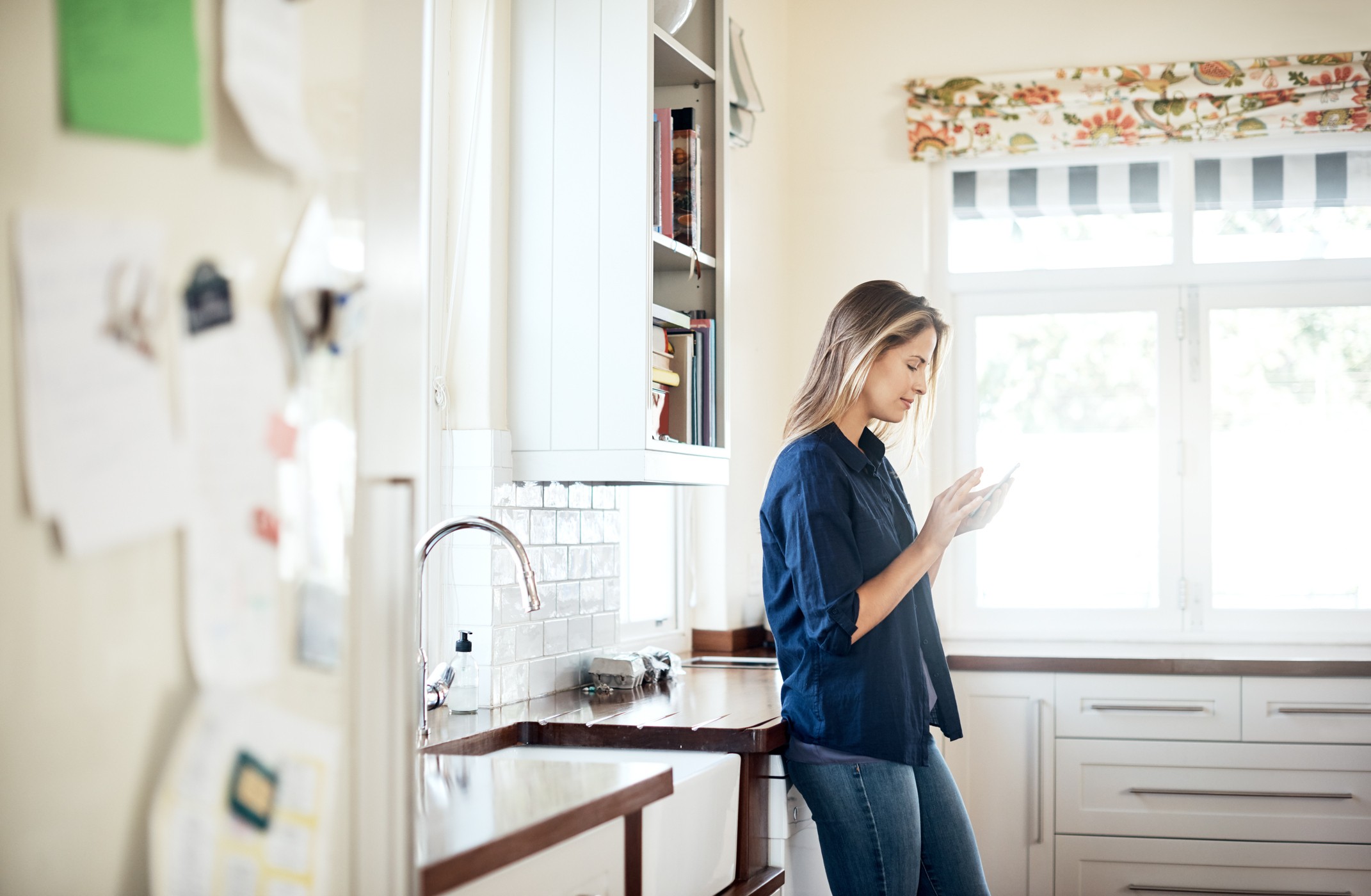 Shot of a young woman using a mobile phone relaxing in the kitchen at home